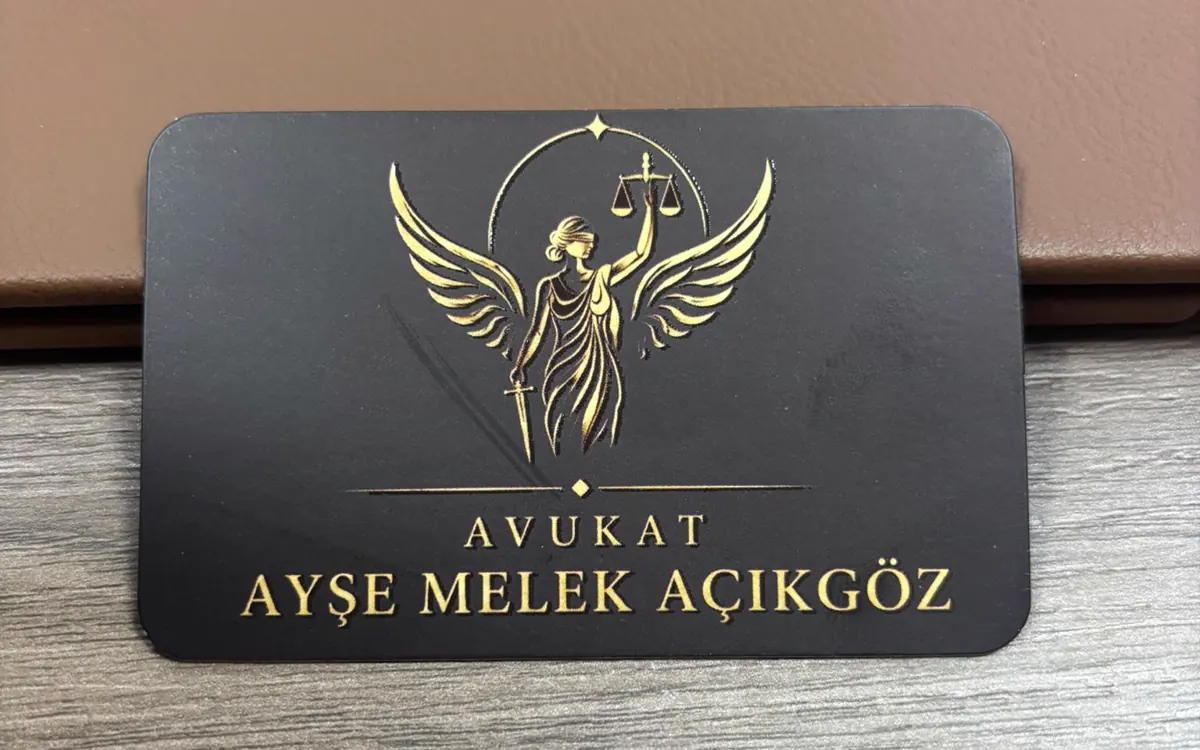Av. A. Melek Açıkgöz kartvizitinin basılı hâli, siyah zemin üzerine altın kanatlı adalet figürü